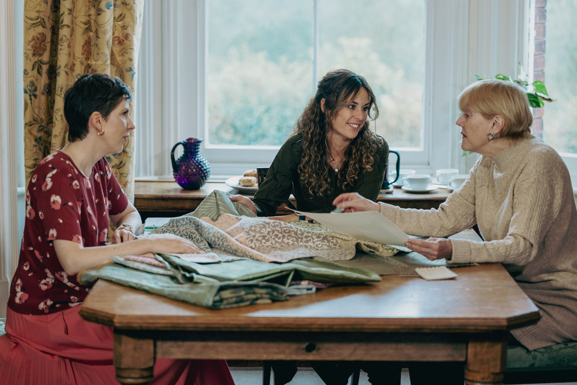 Two account managers talking through a project with a customer, in the Humphries Weaving Showroom. Sitting at a table with a pile of fabric and inspiration.