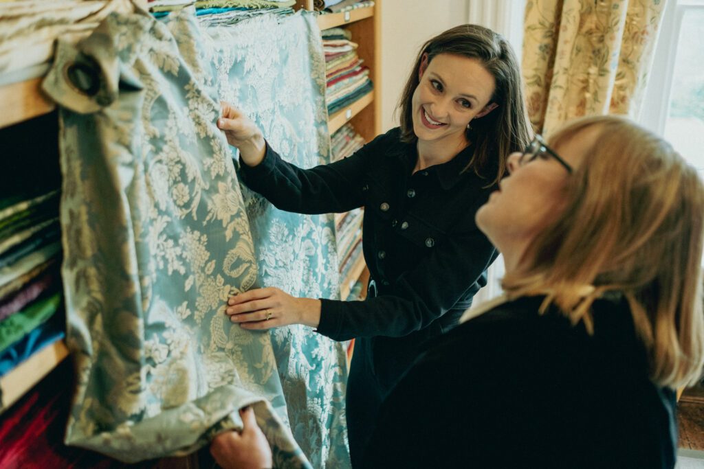 Woman holding blue and white fabric up against shelves to show female customer