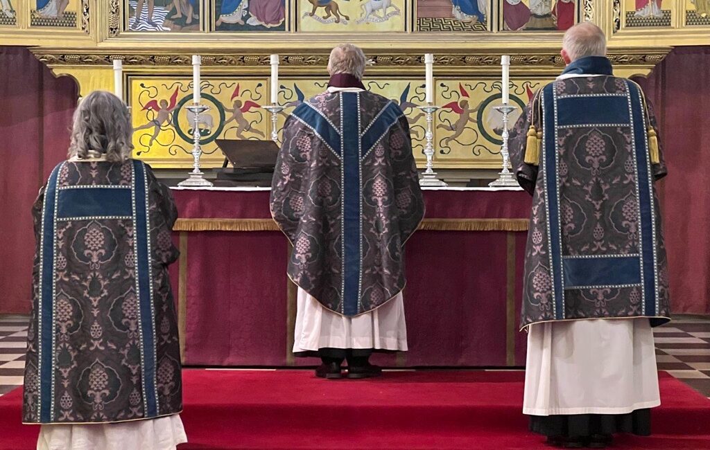 Three figures standing at the back of a church next to a alter wearing St Mark’s cope in the St Marks Cotelin Blue, grey and mulberry silk and linen.