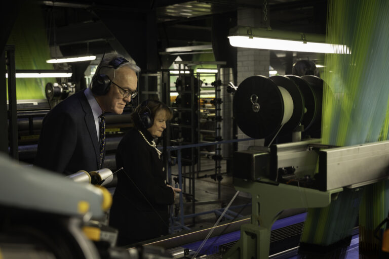 Lady Clare and her Deputy Lieutenant touring the weaving floor, looking at a loom