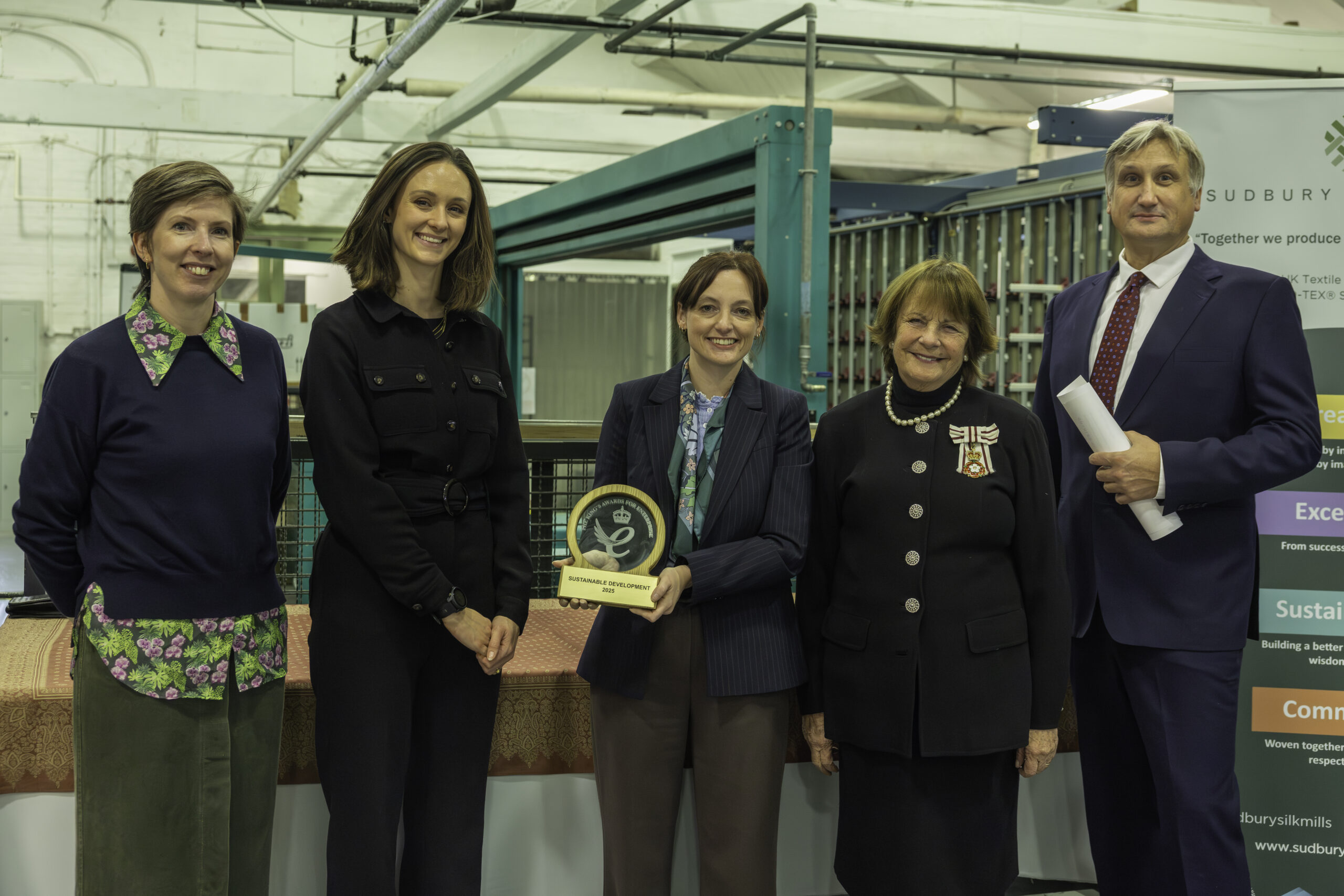 Members of Humphries Weaving and Sudbury Silk Mills posing with Lady Clare whilst holding scroll and trophy for King's Award