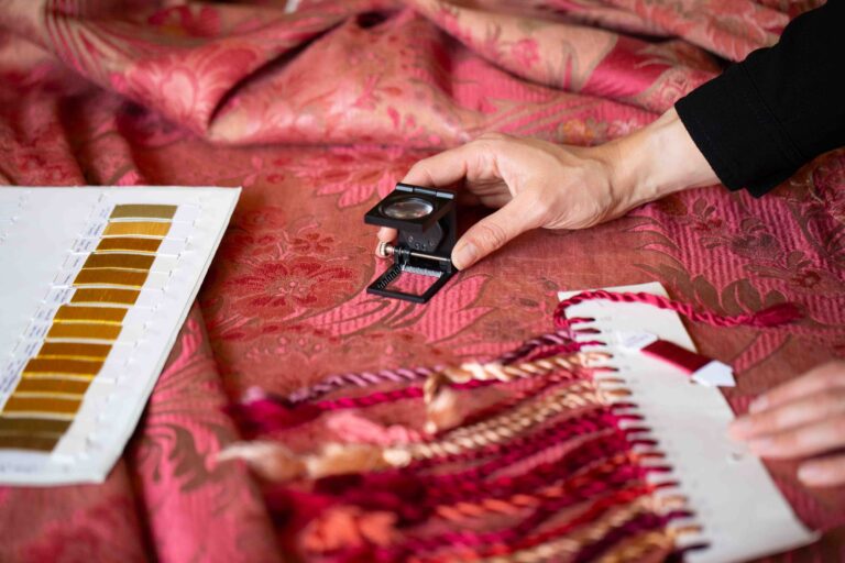 inspecting archive red fabric with a pick glass, surrounded by yarn tabs