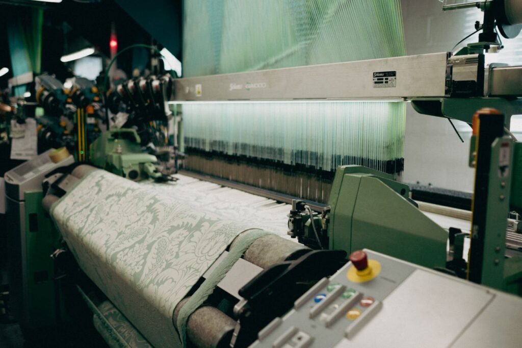 A green weaving loom weaving a pale green and white silk damask design on the factory floor at Humphries Weaving.