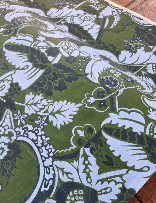 Green, white and black painting with dense floral and leaf pattern draped on a wooden surface
