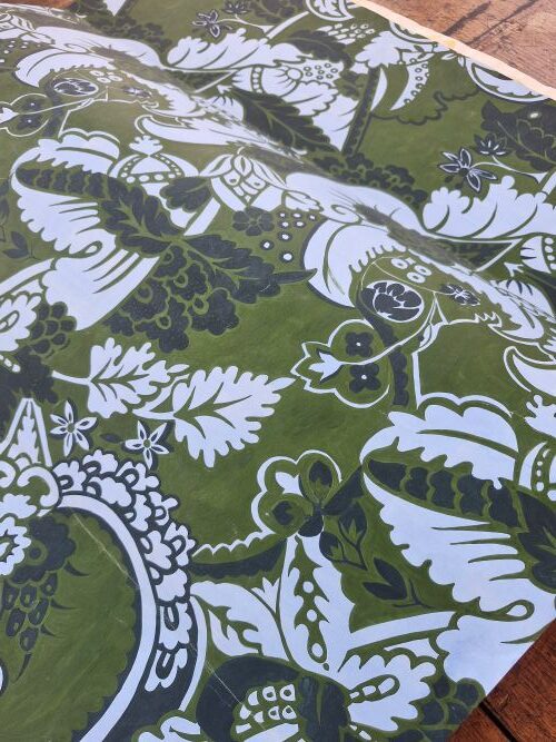 Green, white and black painting with dense floral and leaf pattern draped on a wooden surface
