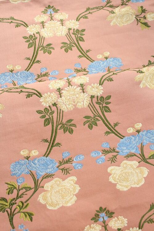 Pink fabric embroidered with trailing green stems and clusters of blue and cream flowers.