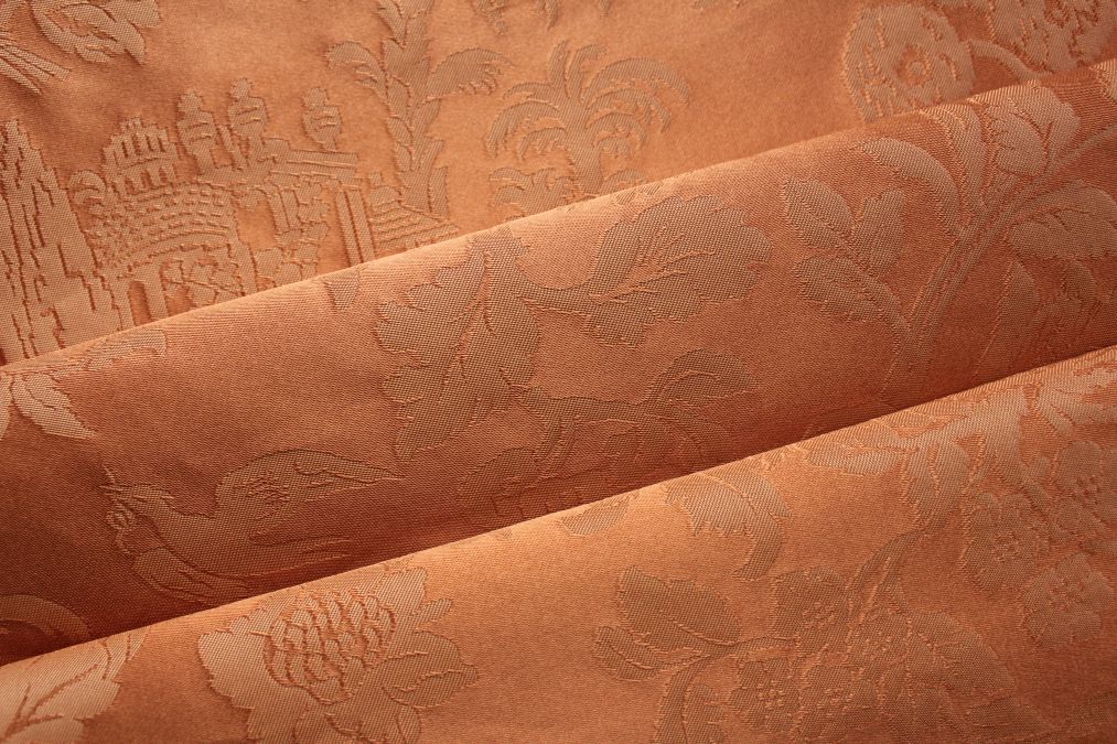 Close-up of folded terracotta jacquard fabric with woven floral, bird and architectural motifs